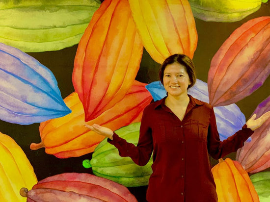 Conexion Chocolate founder Jenny Samaniego standing in her office in front of cocoa pods mural